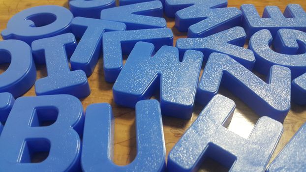 Set of plastic alphabet letters placed on a wooden floor. Alphabet set is used for educating children to learn words and language