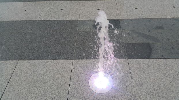 Beautiful and colorful light water fountain over concrete floor. Colorful water shape on fountain with grey background.