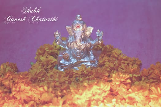 oil lamp illuminated in front of lord ganesha idol with flowers and shubh ganesh chaturthi text