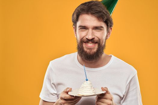 Handsome man with a beard and in a cap celebrating a birthday party yellow background. High quality photo