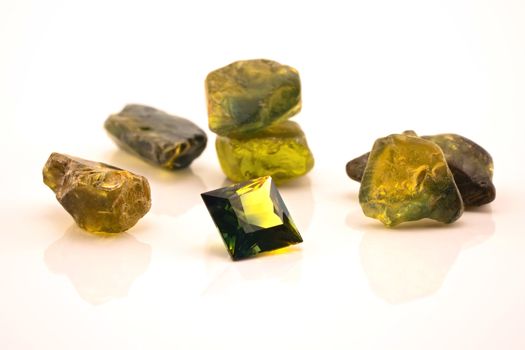 One square facet cut yellow green sapphire surrounded with uncut natural sapphires, isolated on a white background