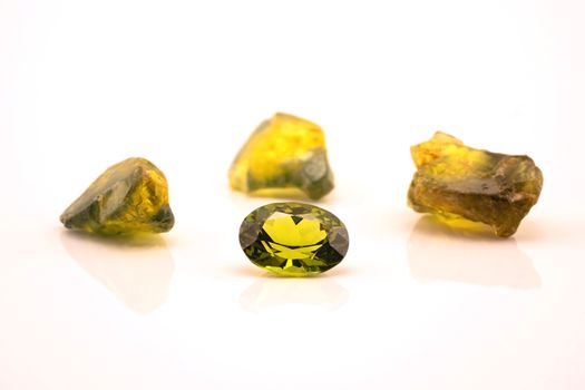 One oblong facet cut yellow green sapphire with three uncut natural sapphires of a similar colour, isolated on a white background