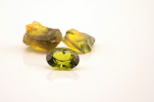 One oblong facet cut yellow green sapphire with two uncut natural sapphires of a similar colour, isolated on a white background