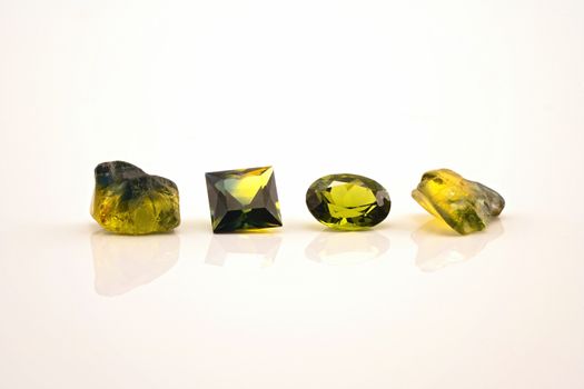 Two facet cut yellow green sapphire with two uncut natural sapphires of a similar colour, isolated on a white background