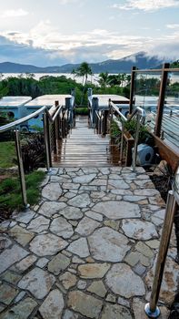 Pathway of paved stone and timber with steel railings leading down to boat shaped accommodation at a tropical coastal resort