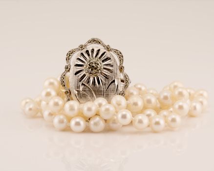 A vintage silver marcasite broach amongst lustrous pearls on a white background