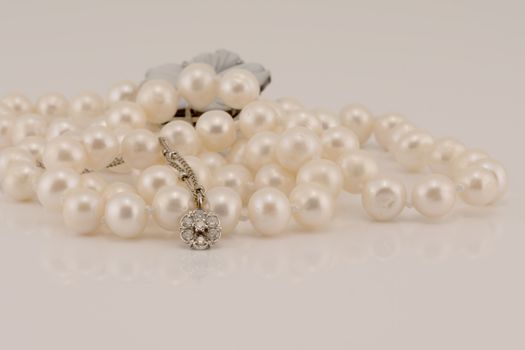 A flower design diamond and white gold pendant nestled in front of lustrous pearls, isolated on a white background