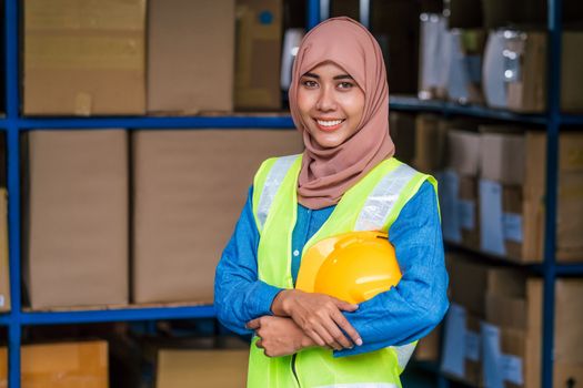 Portrait of Muslim worker woman wearing Hijab and standing and holding hard helmet in local warehouse before start her job, business and industry, business reopening after Covid19 outbreak