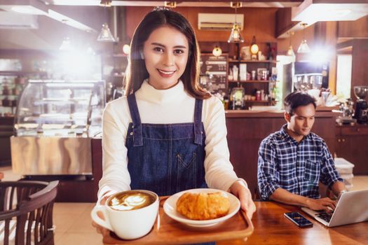 Asian Barista of Small business owner serving a cup of coffee and Croissants bakery to young customer at the table in coffee shop,Small business owner and startup in coffee shop and restaurant concept