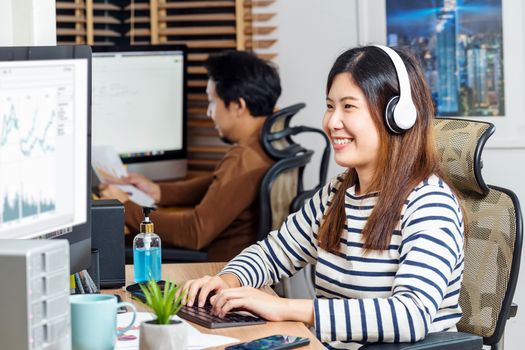 Couple of Asian colleagues smiling and working with computer in Home office when Covid-19 pandemic, Coronavirus outbreak,education and Social distancing, new normal and home office concept