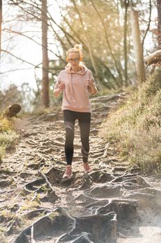 Active sporty woman listening to the music while running in autumn fall forest. Female runner training outdoor. Healthy lifestyle image of young caucasian woman jogging outside.