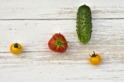 red tomato, two yellow small tomatoes and a cucumber, top view