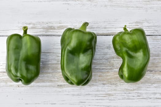 three pods of green bell peppers on a wooden vintage table, top view