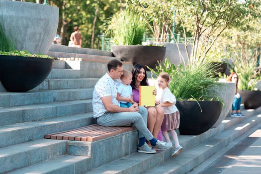 Happy young family with two kids sitting in the park reading a book. Happy parenting concept