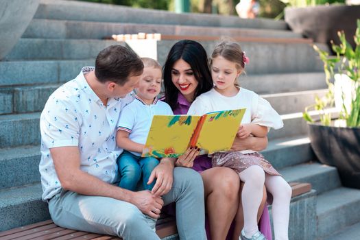 Happy young family with two kids sitting in the park reading a book. Happy parenting concept