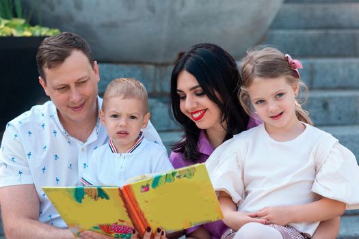 Happy young family with two kids sitting in the park reading a book. Happy parenting concept