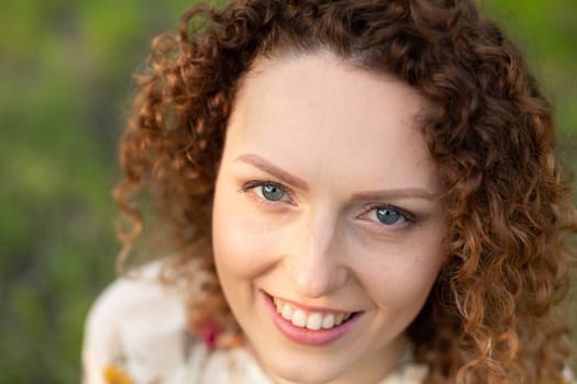 Close up portrait of young smiling attractive woman with curly hair in green flowering spring park. Pure emotions