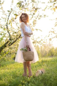 Young attractive woman with curly hair walking in a green flowered garden at sunset. Spring romantic mood.