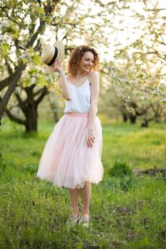 Young attractive woman with curly hair walking in a green flowered garden. Spring romantic mood.