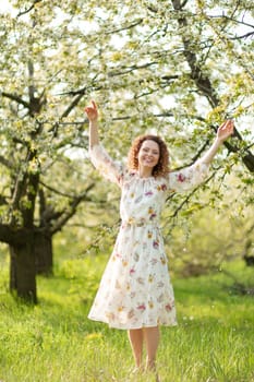 Young attractive girl walks in spring green park enjoying flowering nature.