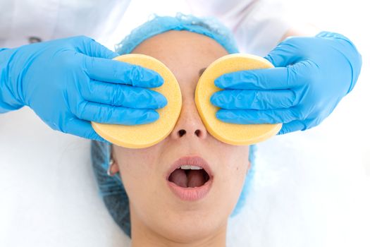 A woman, a professional doctor, a beautician cleanses the patient's face with sponges before applying the mask for skin care.