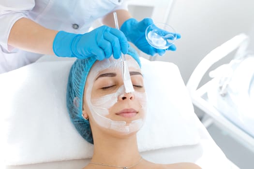 Woman professional doctor beautician applies a mask on a patient's face for skin care. Cosmetic procedures for skin rejuvenation and nutrition.