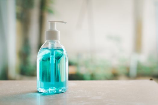 Blue alcohol in bottle pump on a wooden table in front of the shop for customer washing and cleaning hand. Hygiene and health care concept. 