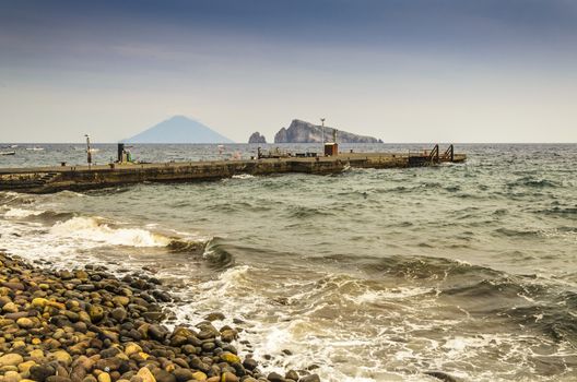 Rocky coast boarding pier of the island of panarea and in the background the volcano Stromboli and two rocks emerging from the Tyrrhenian Sea