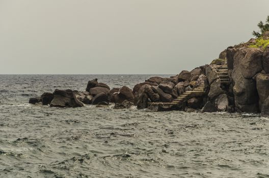 Coast of rocks between which you see the stairs to a small pier on the island of panarea on the Tyrrhenian Sea