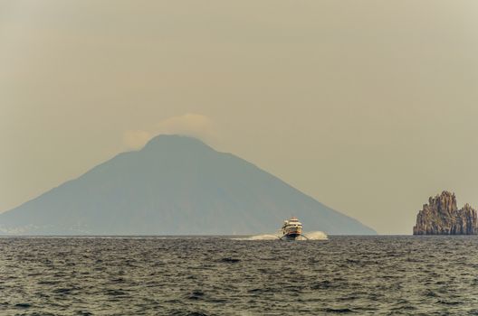 Sea tyrrhenian  boat catamaran rock volcanic emerging from the sea and in the background volcano stromboli smoking from the island panarea