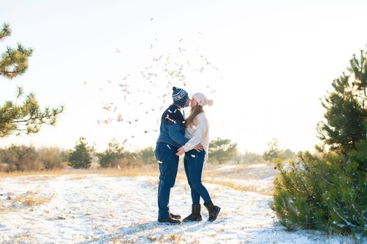 The guy with the girl kiss in the winter in the woods against the background of falling candy. Romantic winter atmosphere.