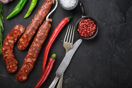 Spanish chorizo sausage slices with herbs and spices on balck background, top view with copy space.