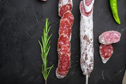Dry cured fuet salami sausage slices on balck background, top view with copy space.