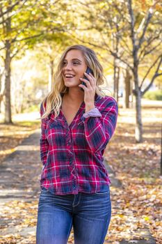 A gorgeous blonde model talks on her cellphone on an autumn day outdoors in a park
