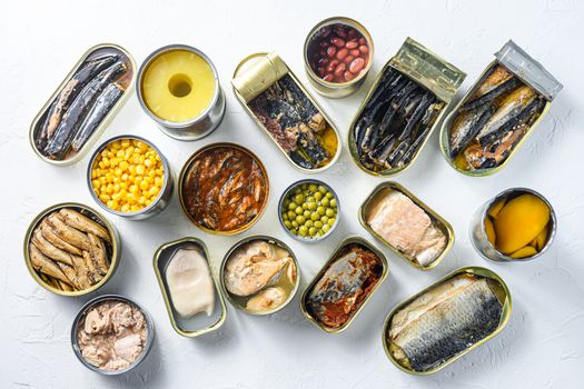 Assortment of canned preserves food in cans. On white rustic background conserve Saury, mackerel, sprats, sardines, pilchard, squid, tuna pinapple, corn, peas, mango , beans, top view