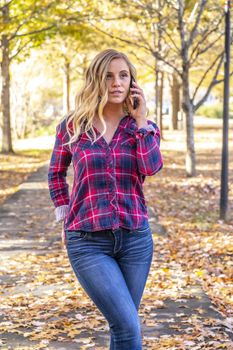 A gorgeous blonde model talks on her cellphone on an autumn day outdoors in a park
