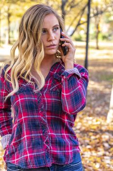 A gorgeous blonde model talks on her cellphone on an autumn day outdoors in a park