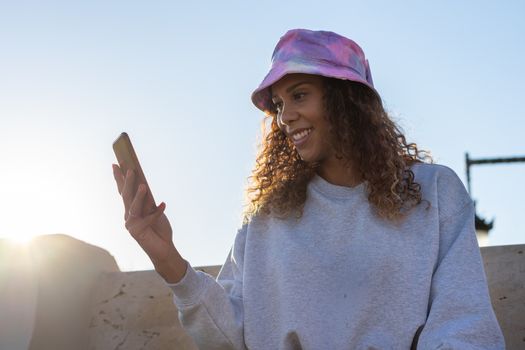 Portrait of an attractive young black woman sitting and talking with the mobile phone outdoors with her mask off. Concept communication