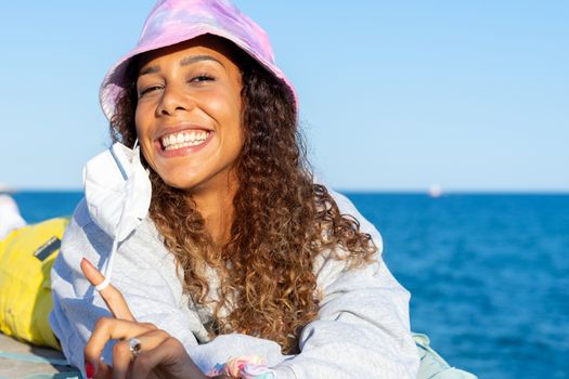 Portrait of an attractive young black woman lying relaxed on the beach with her mask off. Looking to the camera