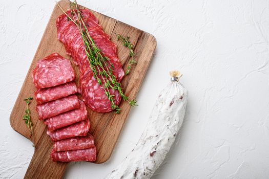 Salchichon whole and sliced cuts, spanish sausage on white surface, top view with copy space.