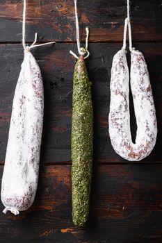 Spanish dry sausages hang from a rack at market on dark wood background.