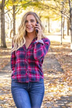 A gorgeous blonde model talks on her cellphone on an autumn day outdoors in a park