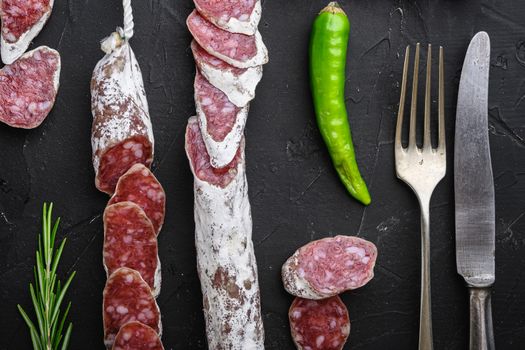 Dry cured fuet salami sausage slices on black textured background.