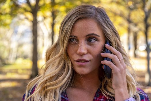 A gorgeous blonde model talks on her cellphone on an autumn day outdoors in a park