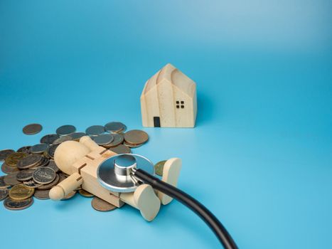 A wooden doll lying on a pile of money with a stethoscope And there is a model wooden house nearby. Concept of checking financial condition and debt.