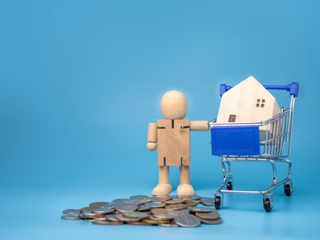 Coins and wooden dolls that Stand next to the shopping cart With a model wooden house on top And has a blue background. Home buying and selling ideas