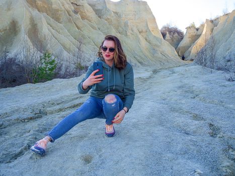 Hiker on mountain top with smartphone. Woman is standing and taking a picture on smartphone. Abandoned Quarry Of Rummu, Estonia. Scenic View Of Land Against Clear Blue Sky. Panoramic View.