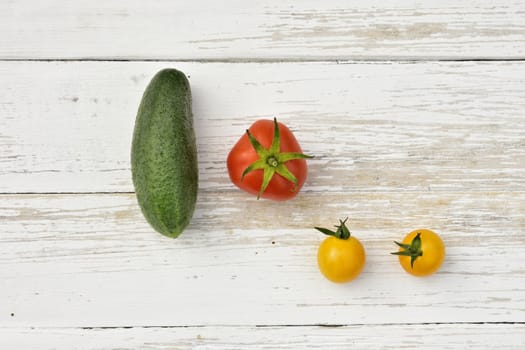 red tomato, two yellow small tomatoes and a cucumber on a wooden vintage table, top view