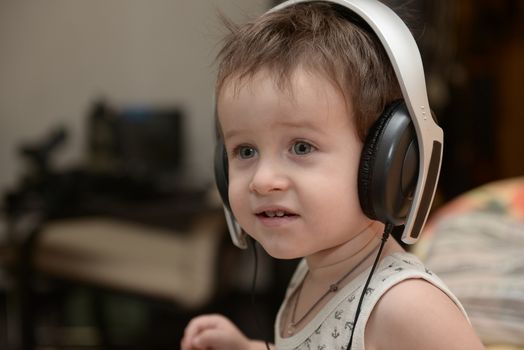 Charming boy listening to music in headphones in a room
