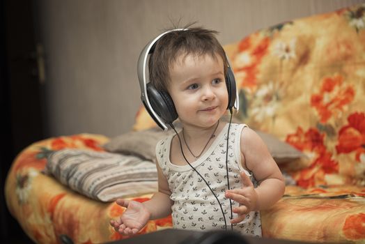 Charming boy listening to music in headphones in a room